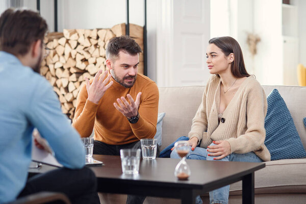Несчастная пара, сидящая на диване на сеансе терапии в кабинете терапевта
