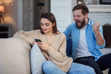 Genç kadın koltukta otururken akıllı telefon kullanıyor ve kocası da arkasından üzülüyor. Akıllı telefon bağımlılığı nedeniyle ailede sorunlar var..