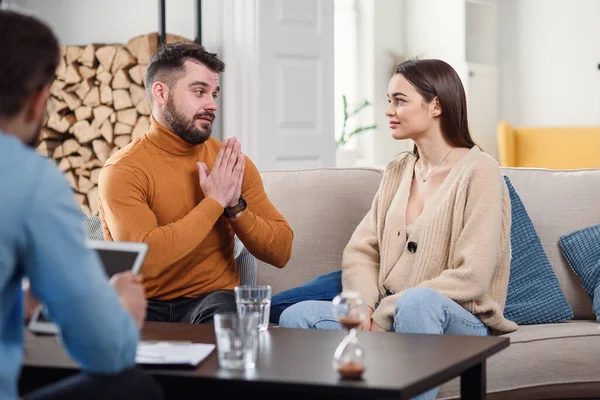 Young loving wife supporting her depressed husband during psychotherapy session with counselor, free space — Stock Photo, Image