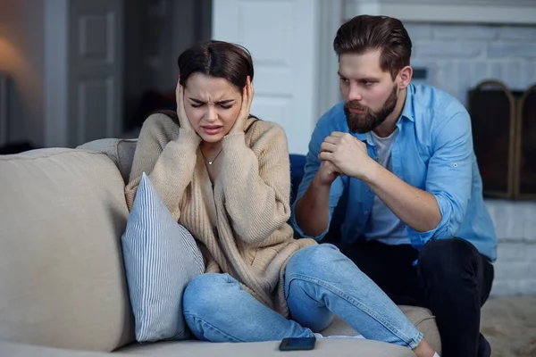 Defenseless upset woman closes her ears while her husband yelling at her sitting behind. Family relationship problems concept. — Stock Photo, Image