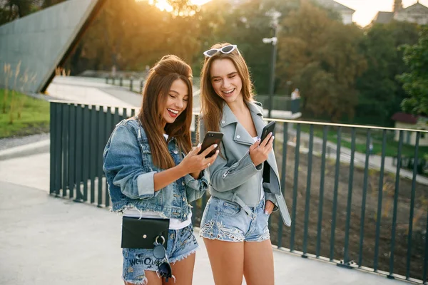 As namoradas usam smartphone enquanto caminham na cidade de manhã. As blogueiras femininas viajam pela Europa. Comunicação moderna tecnologias inteligentes e conceito de amizade . — Fotografia de Stock