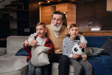 10-15 yaşlarındaki neşeli torunları ile konsantre olmuş yaşlı ve sakallı büyükbabası boş zamanlarını TV 'deki basketbol maçını gözden geçirmeye harcıyorlar.