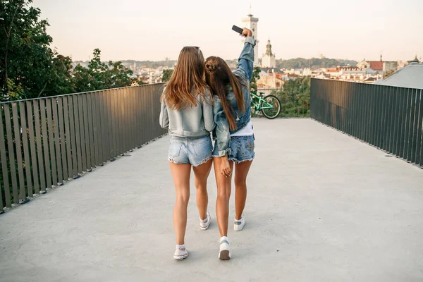 Duas melhores amigas tirando selfie com smartphone quando sentadas no skate enquanto caminham no dia ensolarado do verão. Ao ar livre. Movimento lento — Fotografia de Stock