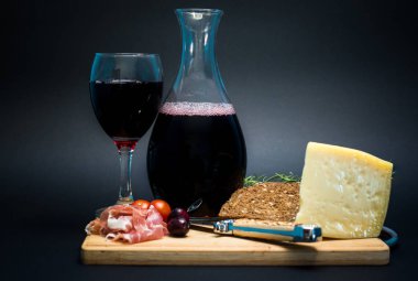 Yavaş yemek ve bir şişe kırmızı şarap ve bir bardak şarap sert sarı peynirli, jambonlu, vişneli domatesli ve zeytinli ahşap bir tepside servis ediliyor. Tepsinin ortasında dekoratif bir av bıçağı var..