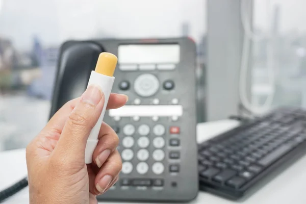 Segure um bálsamo labial amarelo com fundo de escritório — Fotografia de Stock