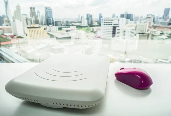 Ponto de acesso branco com mouse roxo na mesa de escritório com vista para a cidade — Fotografia de Stock