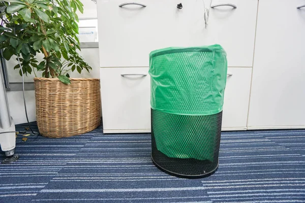 Корзина из нержавеющей стали с зеленым пластиковым пакетом сверху в офисе — стоковое фото
