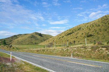 Beton yol boyunca yeşil tepe Lindis Pass Yeni Zelanda'da parlak mavi gökyüzü ile