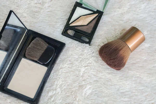 flat lay close up pressed powder and eye shadoe pallete with beauty brush on fur background