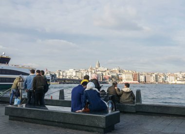 İstanbul / Türkiye - 12 Aralık 2019: Bir grup insan tatillerde Boğaziçi Gemi Turları 'nda sahil kenarında oturuyor