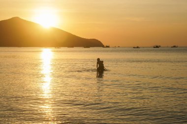 Siluet oğul ve baba altın gün batımında denizde su oynuyorlar.