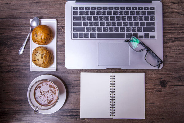 Computer, tea, bread and notebook on wood table