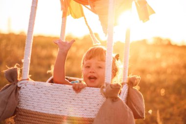 Balon. Çocuk bir seyahat eder. Balon uçuş. Büyük bir balon. Güneşli bir gün. Gün batımında uçuş. Çocuk duygular. Sevinç. Gülmek.
