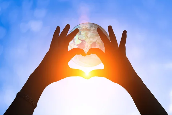 Jorden och händerna under en hjärtformade siluett. Vacker kvinnlig modell njuter av solnedgången. Händer hålla och skydda jorden på natur botten . — Stockfoto