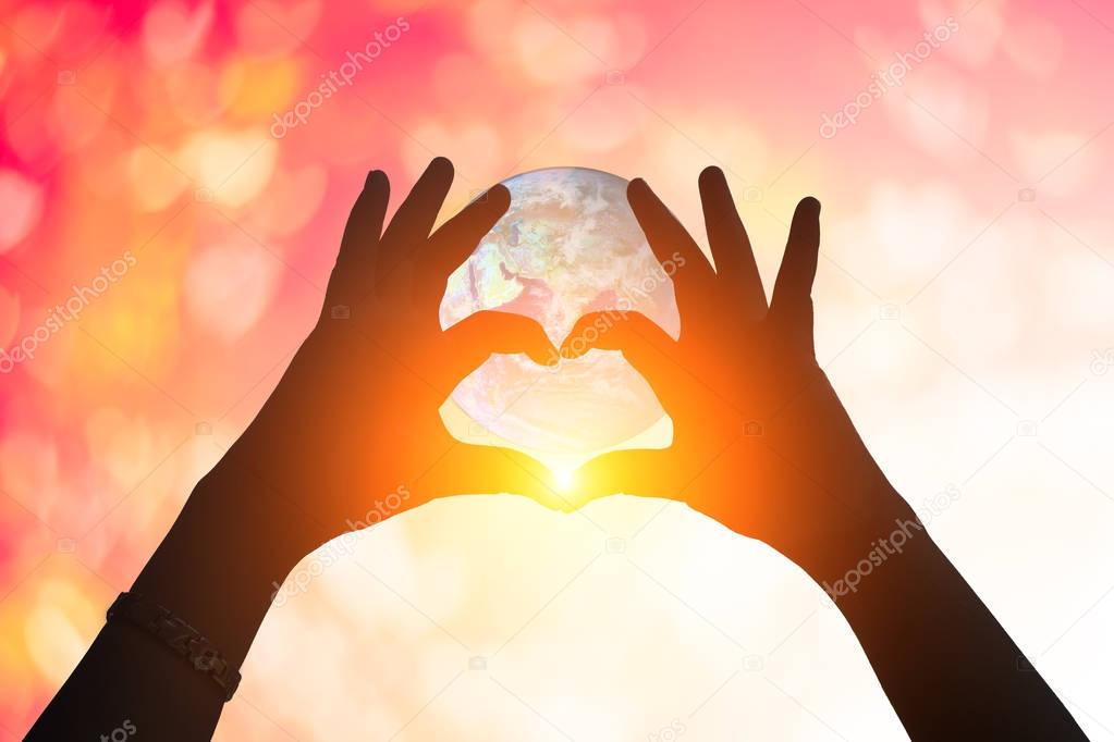 Earth and hands under a heart-shaped Silhouette .Beautiful Female Model Enjoying Sunset  .Hands holding and protect earth on nature background .