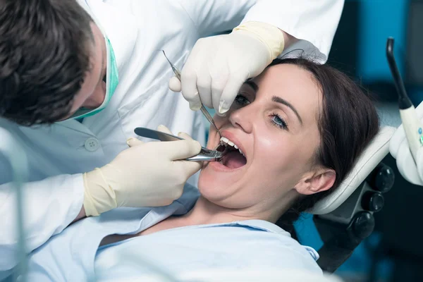 Dentysta bada pacjenta zęby z lustrem usta. — Zdjęcie stockowe