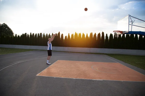 Een man, staan hoog, het voorbereiden om te schieten een basketbal, in een park — Stockfoto