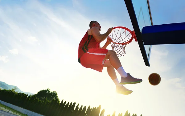 Jovem jogador de basquete dirige para o aro para um mergulho alto voando na frente do céu por do sol . — Fotografia de Stock