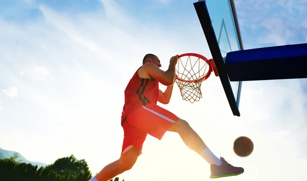 Jeune joueur de basket-ball conduit au cerceau pour un haut vol slam dunk en face du ciel couchant . — Photo