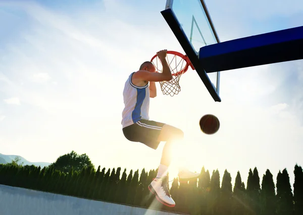 Young basketball player drives to the hoop for a high flying slam dunk in front of sunset sky. — Stockfoto
