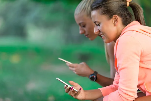Dos mujeres bastante jóvenes en traje deportivo usando un teléfono inteligente — Foto de Stock