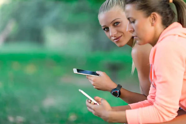 Dos mujeres bastante jóvenes en traje deportivo usando un teléfono inteligente — Foto de Stock