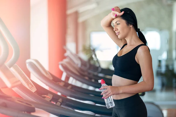 Mulher com garrafa de água exercitando-se em esteira na academia — Fotografia de Stock