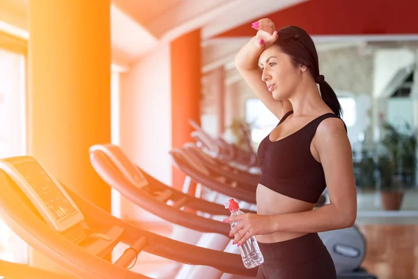 Vrouw met fles water uit te oefenen op de loopband in de sportschool — Stockfoto