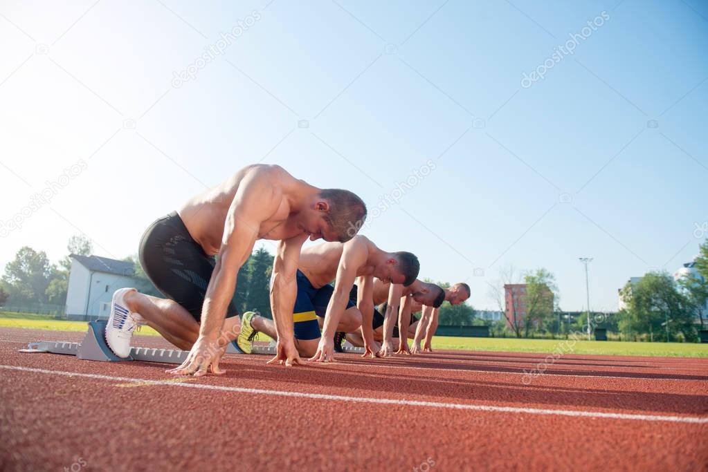 Male athletics runners on starting line without shirts.