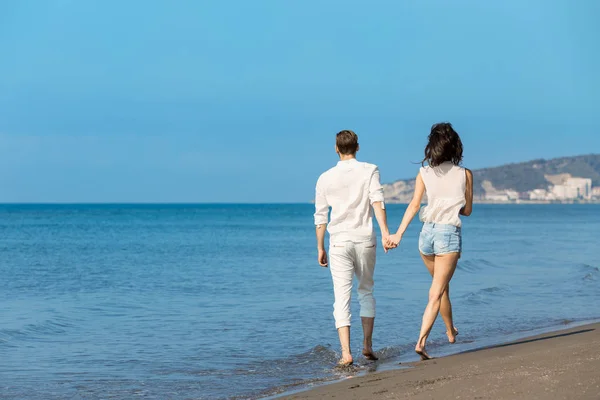 Jong koppel wandelen op het strand glimlachen — Stockfoto