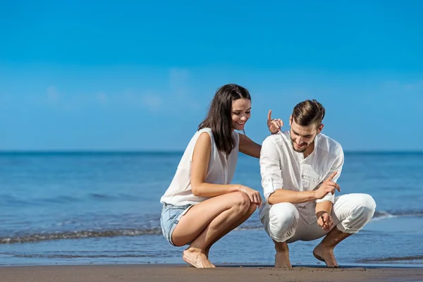 Romantic young couple draw shapes on the sand while on honeymoon. — Stock Photo, Image