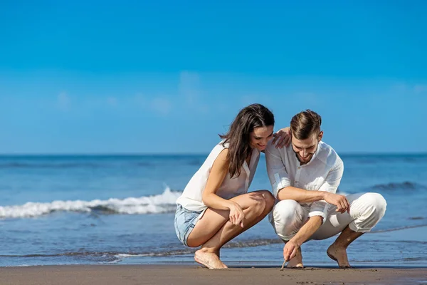 Romantisches junges Paar zeichnet Formen auf dem Sand während der Flitterwochen. — Stockfoto