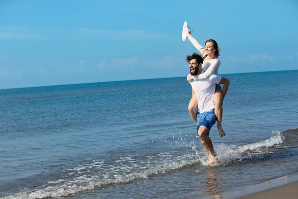 Ein Typ, der ein Mädchen am Strand auf dem Rücken trägt — Stockfoto