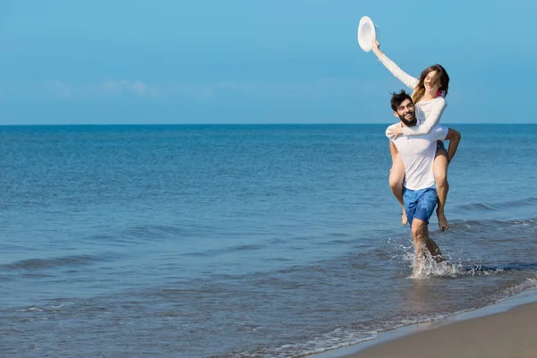 Ein Typ, der ein Mädchen am Strand auf dem Rücken trägt — Stockfoto