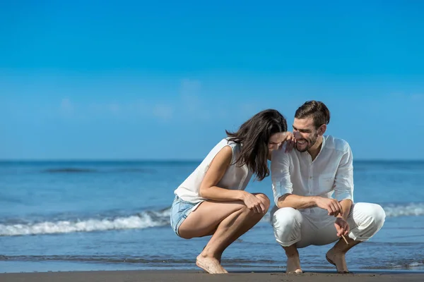 Romantische jong koppel tekenen vormen op het zand terwijl op huwelijksreis. — Stockfoto