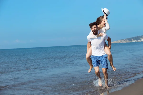 A guy carrying a girl on back at beach — Stock Photo, Image