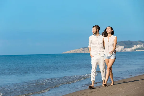 Pareja joven caminando en la playa sonriendo — Foto de Stock