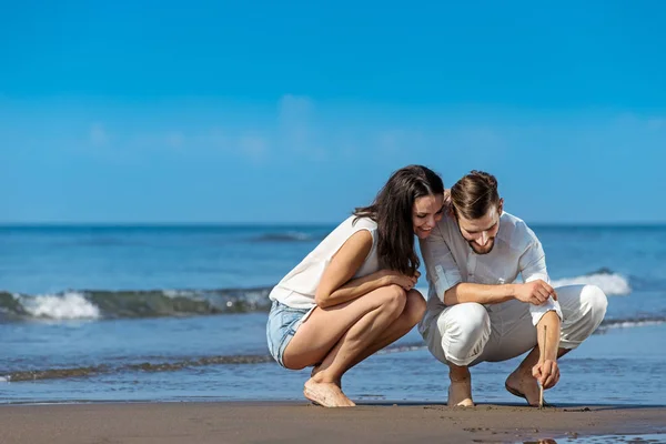 Romantische jong koppel tekenen vormen op het zand terwijl op huwelijksreis. — Stockfoto