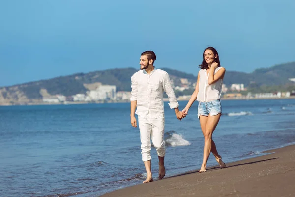 Jeune couple marchant sur la plage souriant — Photo