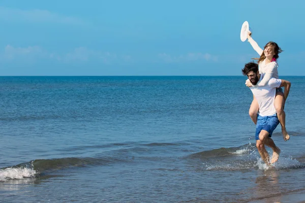 Um cara carregando uma garota na praia — Fotografia de Stock