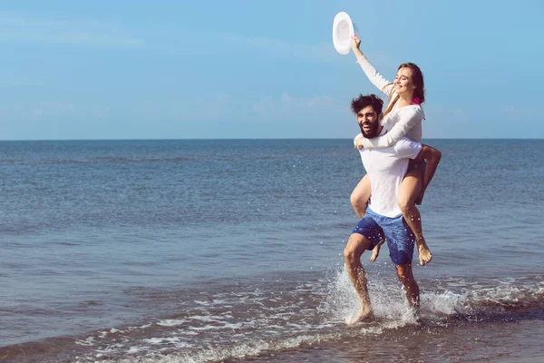 Een man met een meisje op rug op strand — Stockfoto