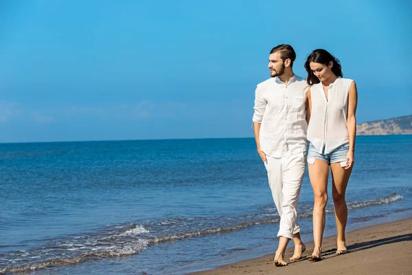 Jong koppel wandelen op het strand glimlachen — Stockfoto