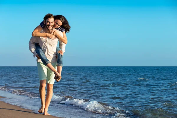Man geven piggy terug naar vriendin op het strand — Stockfoto