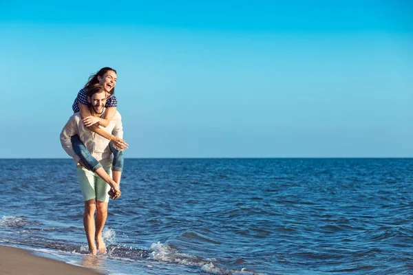 Mann gibt Freundin am Strand Huckepack zurück — Stockfoto