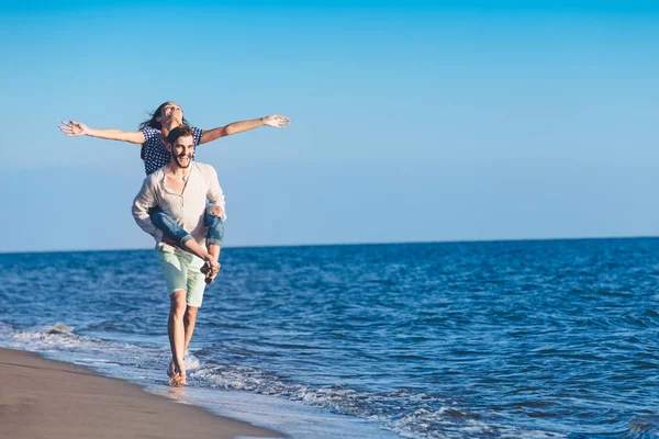 Man geven piggy terug naar vriendin op het strand — Stockfoto