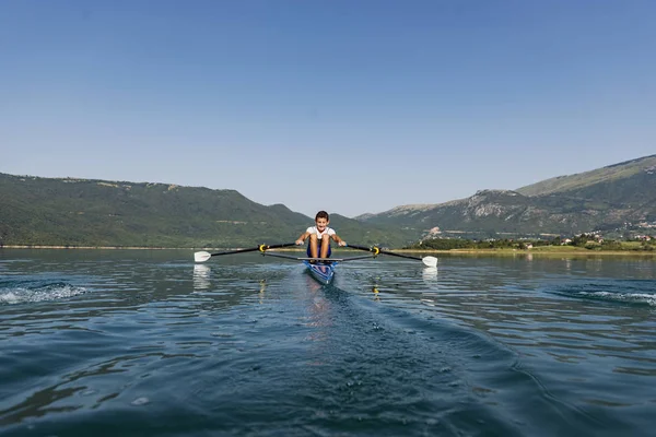 Un joven solo scull remo competidor paletas en el tranquilo lago —  Fotos de Stock