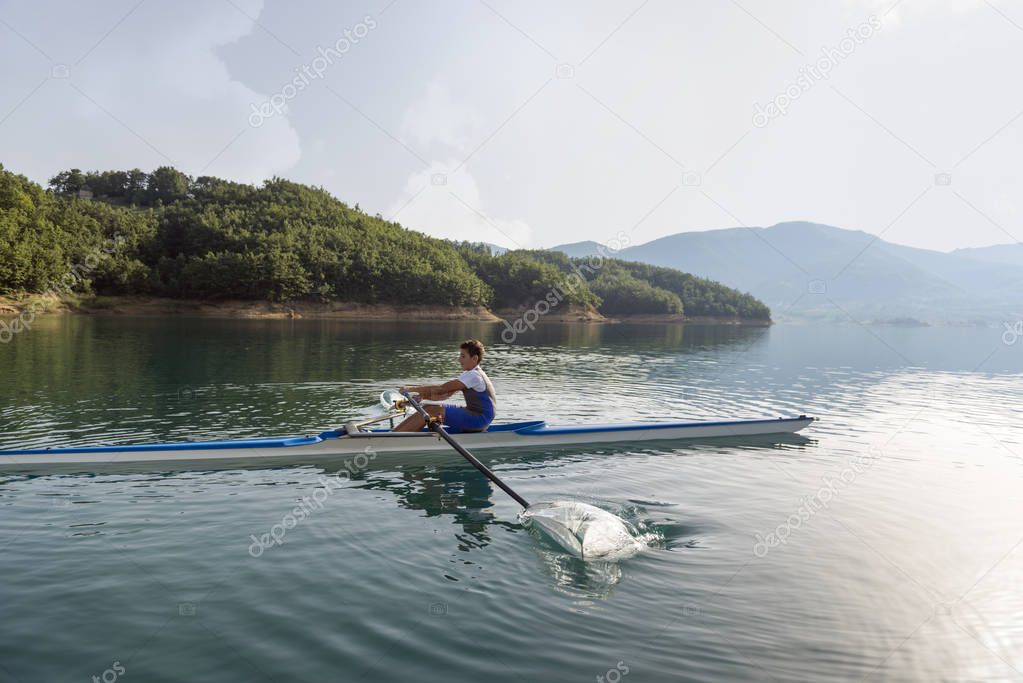 Young single scull rowing on lake