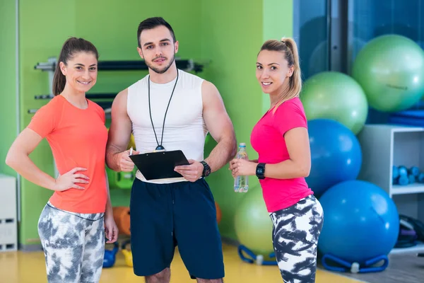 Mulheres jovens e personal trainer no ginásio — Fotografia de Stock