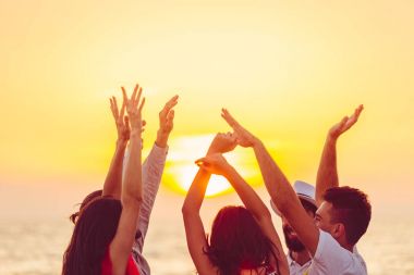 people dancing at the beach with hands up.  clipart