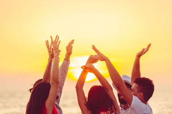 Menschen tanzen mit erhobenen Händen am Strand. — Stockfoto